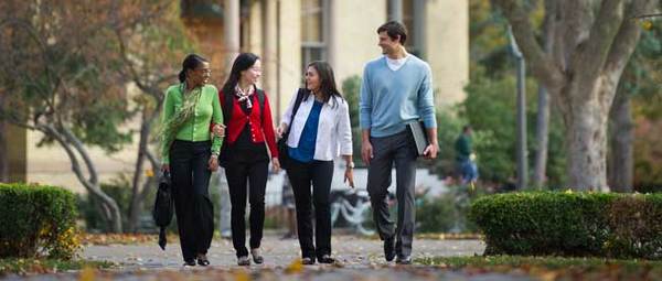 Four students walk down a path toward the camera on Notre Dame's campus.