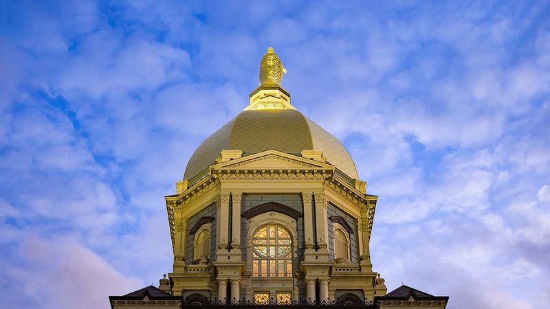 Looking up at Notre Dame's golden dome against a background of blue sky and clouds.