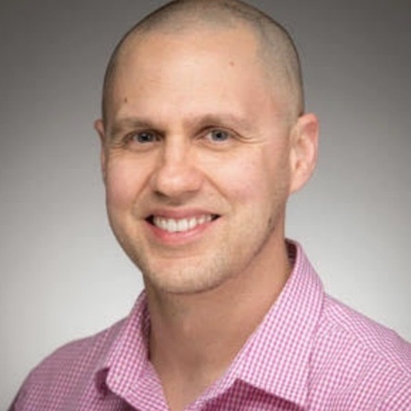 Headshot of Alan Huebner wearing a pink patterned button down shirt.