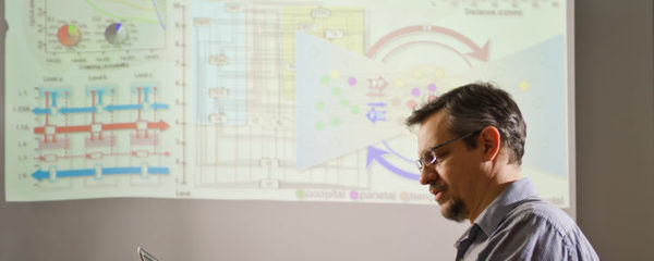 A profile of a man looking to the left with charts and data displayed on a screen behind him.