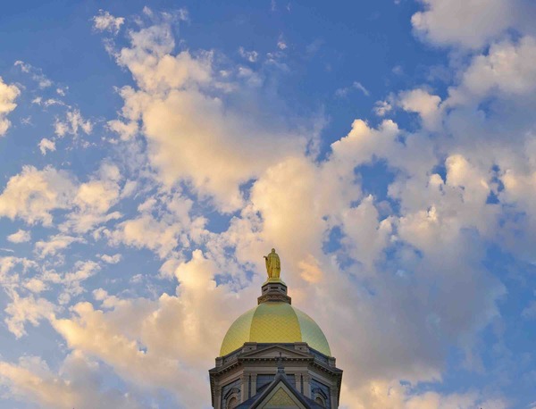 Notre Dame's golden dome surrounded by sky and clouds.