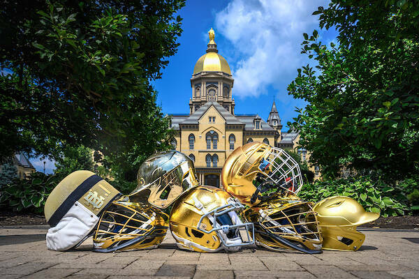 A pile of golden Notre Dame football helmets sitting in front of the Main Building on Notre Dame's campus.